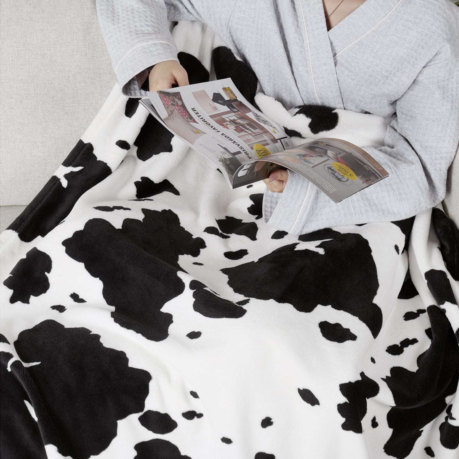 Person reads under a cow print blanket #color_Black White