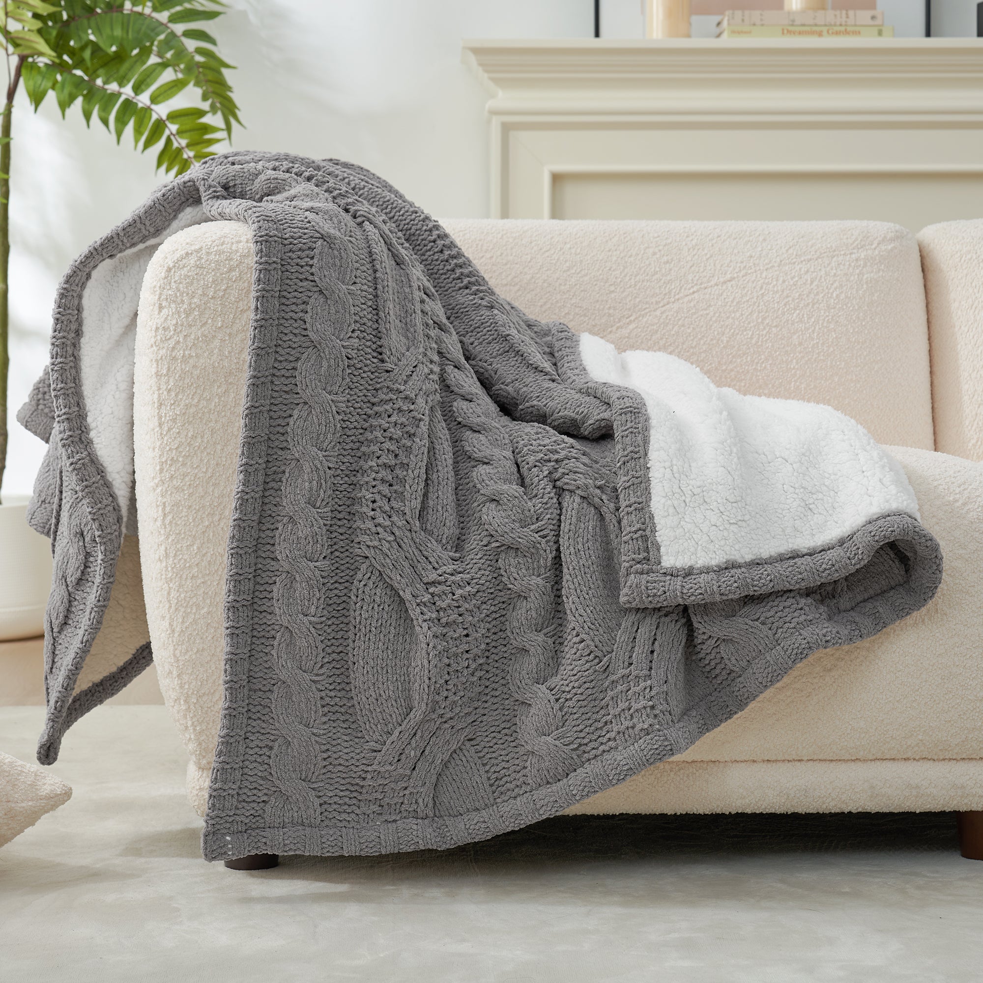 Gray cable knit blanket draped over a beige sofa in a living room setting. #Color_Grey