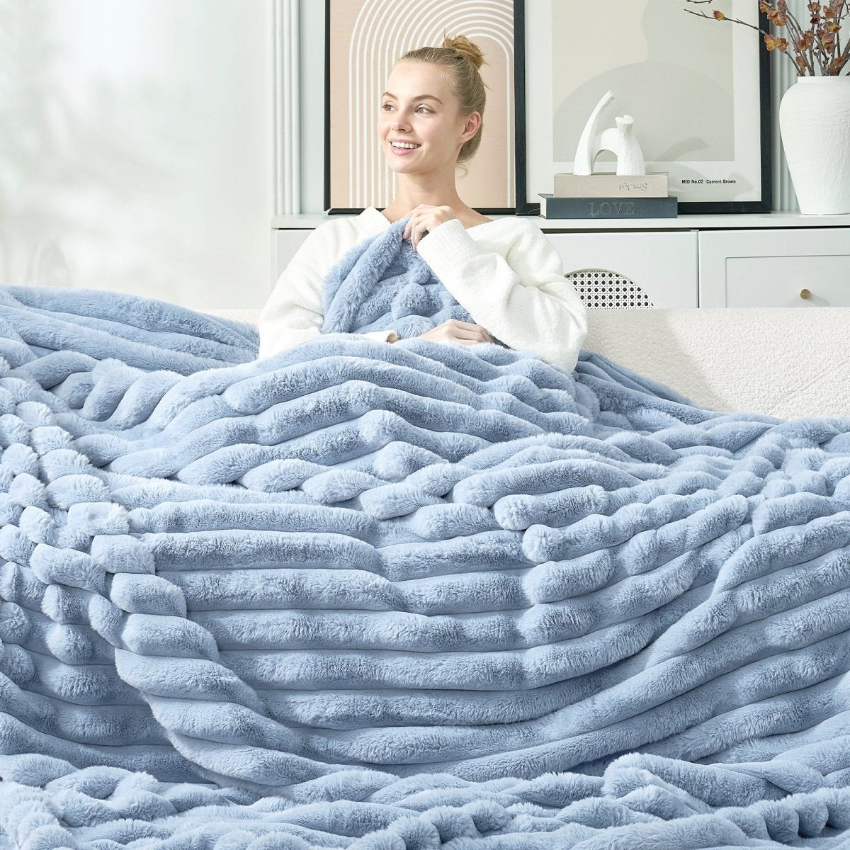 Woman wrapped in a large light blue striped faux fur throw blanket in a cozy living room. #color_Misty Blue