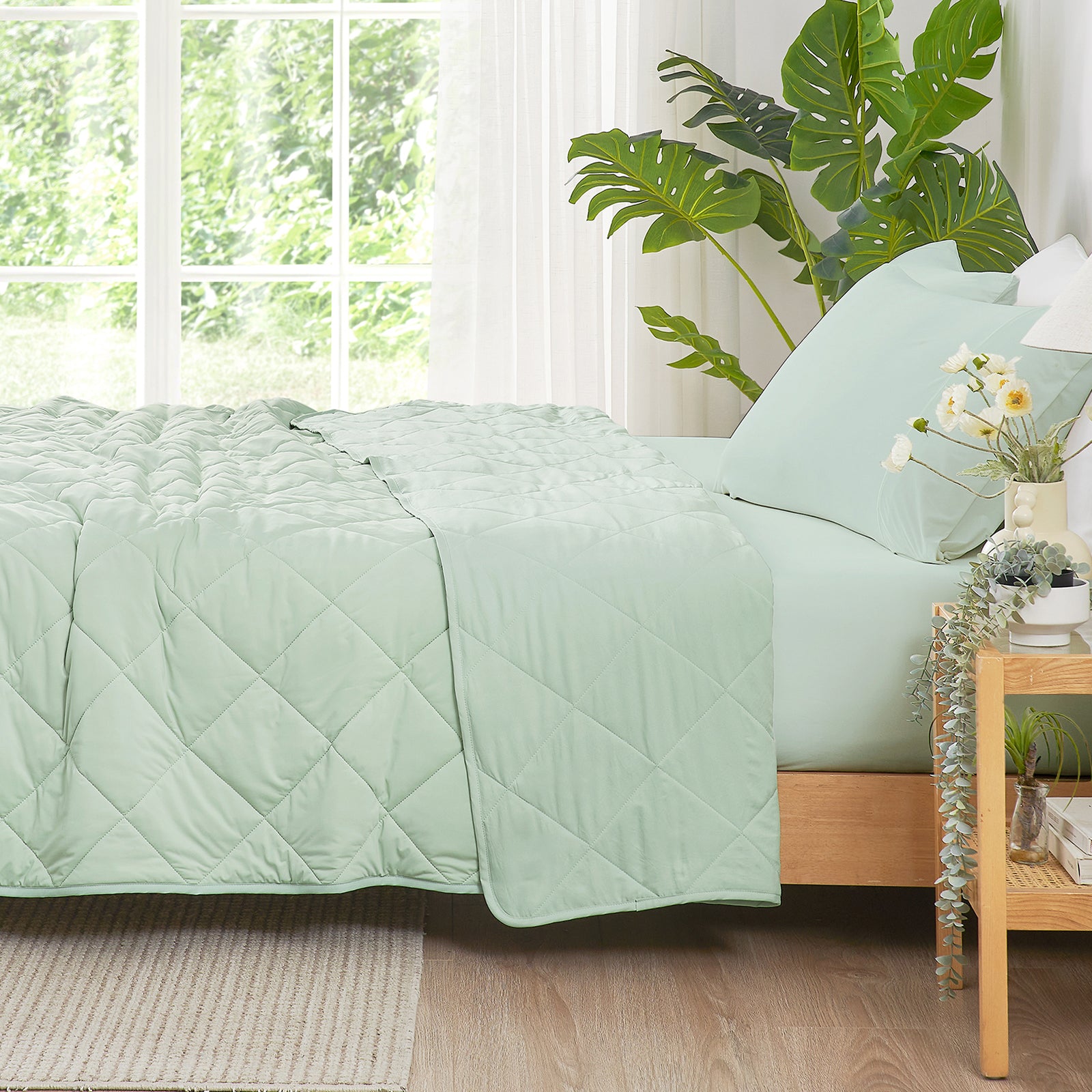 Bed with light green quilt and pillows in a bright bedroom with plants and a window.  #color_Mint Green