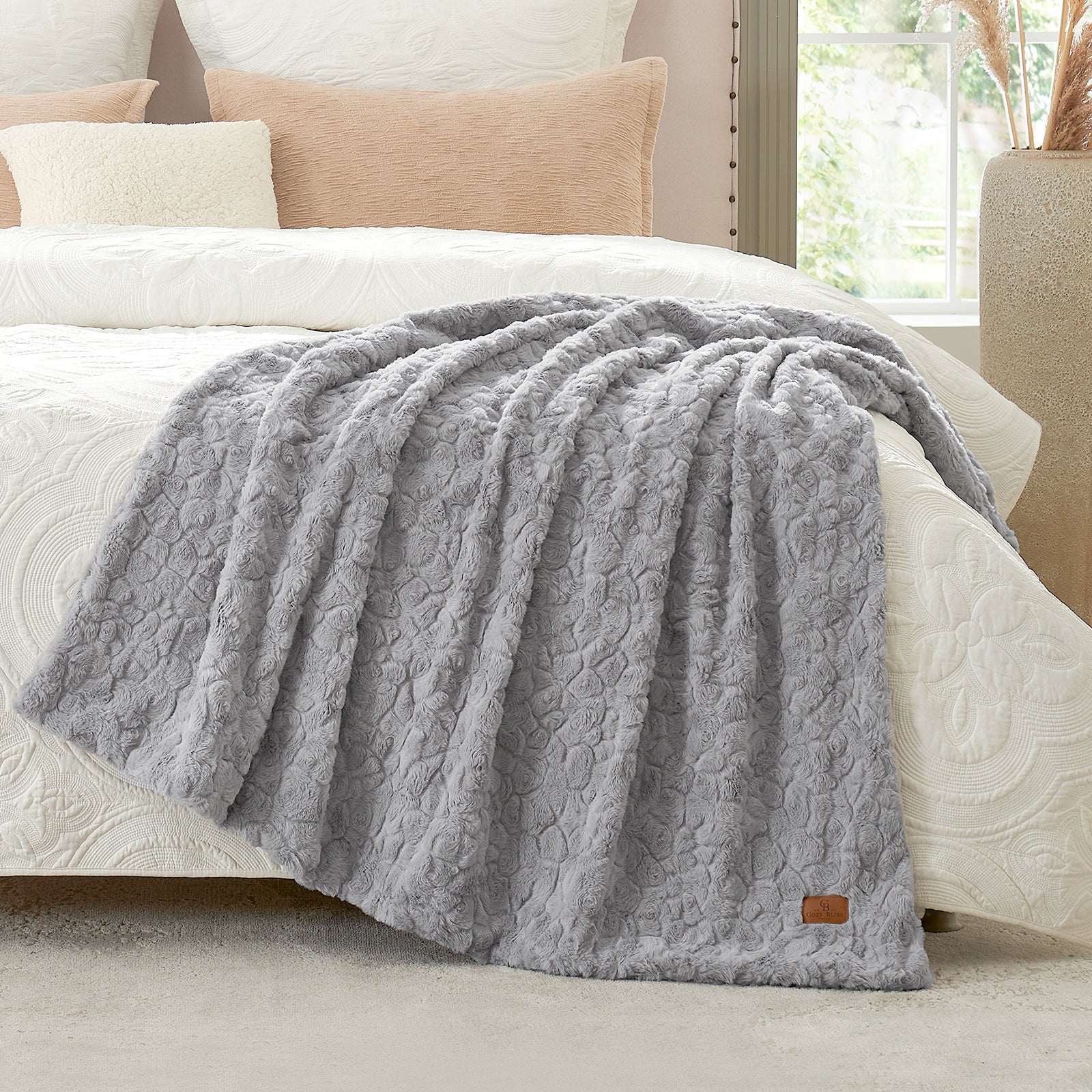 Gray textured blanket on a bed with beige pillows and a lamp in the background  #color_Grey