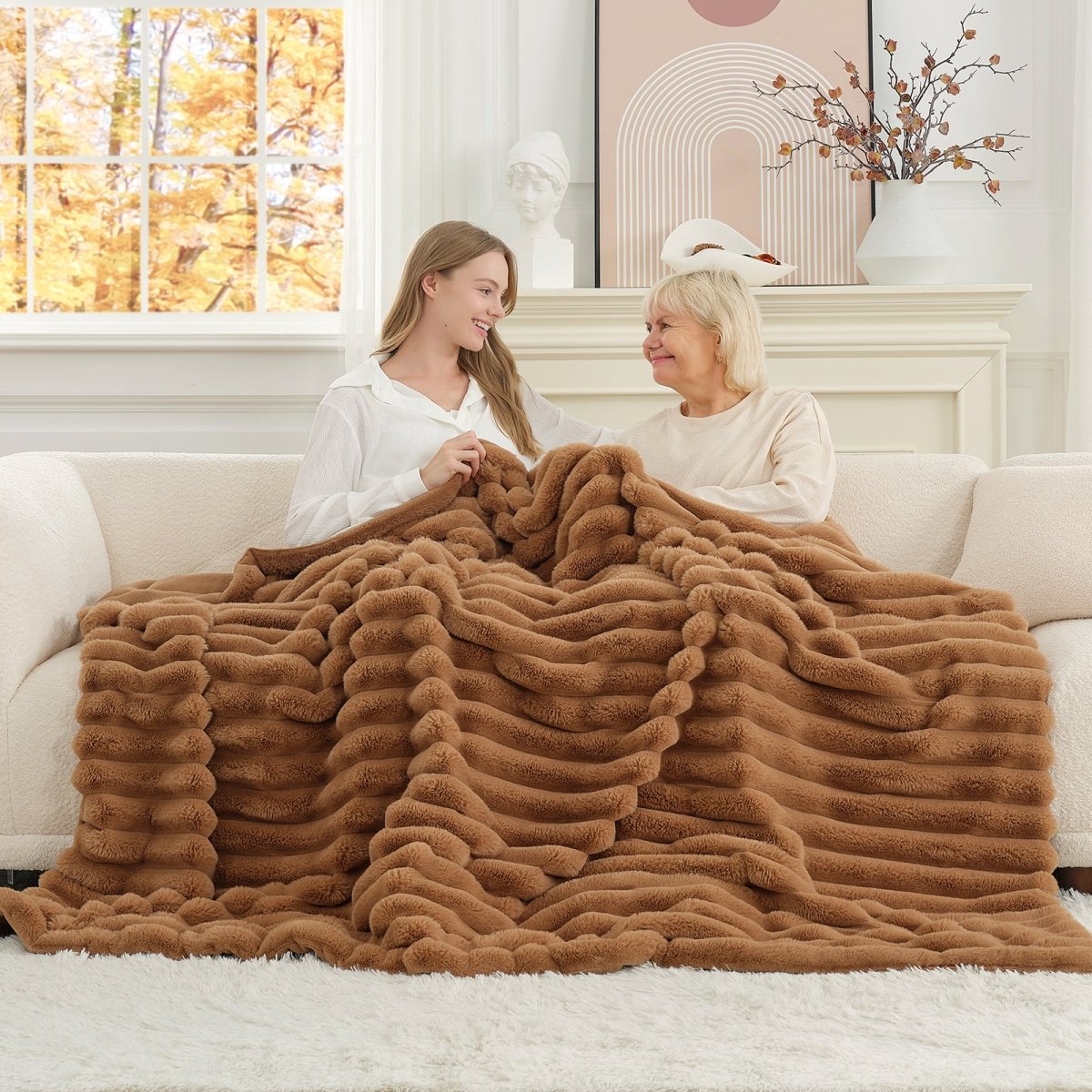 Mom and daughter sitting on a couch under a brown fuzzy blanket in a cozy living room. #color_Toasty Brown