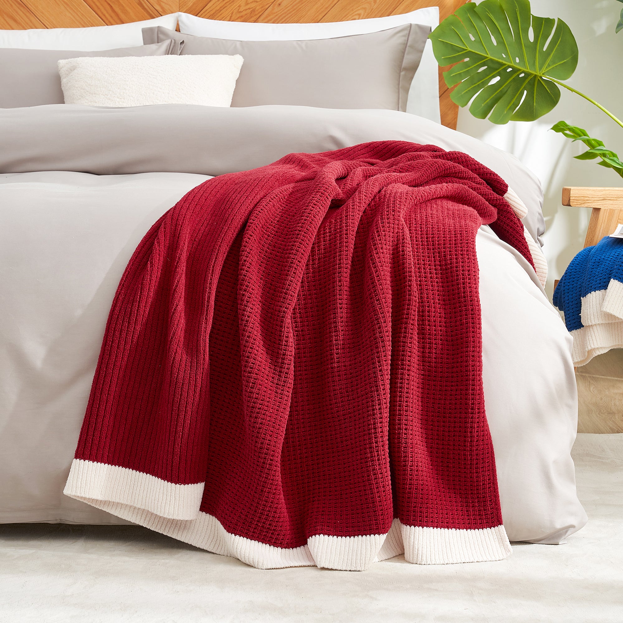 Red blanket on a bed with white bedding and a plant in the corner. #color_Red