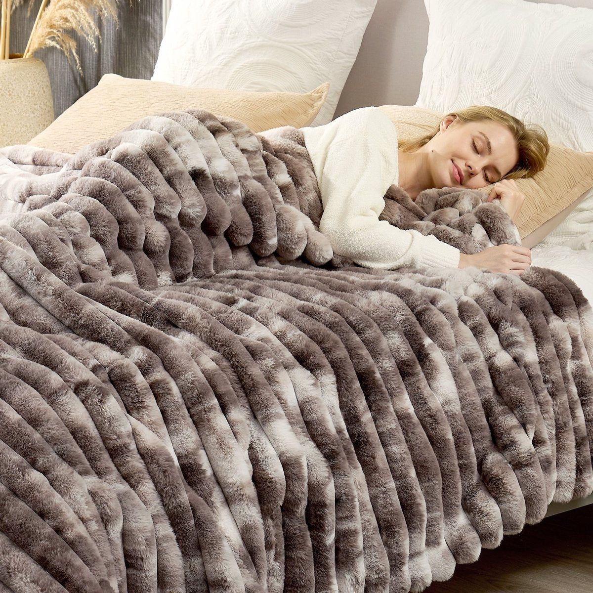Woman lying on a bed under a fluffy taupe blanket. #color_Tie-dye Taupe