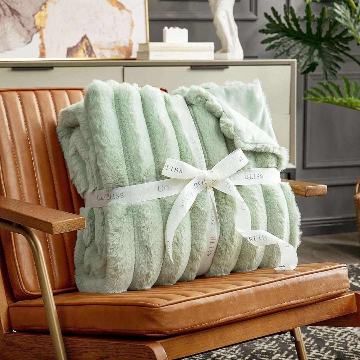 Cozy Bliss sage green faux fur throw blanket on brown leather chair, perfect for gifting. Cozy bedding. #color_Sage Green