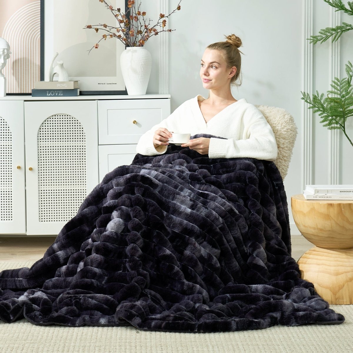 Woman sitting on a couch with a black textured blanket draped over her, in a cozy living room setting. #color_Tie-dye Black