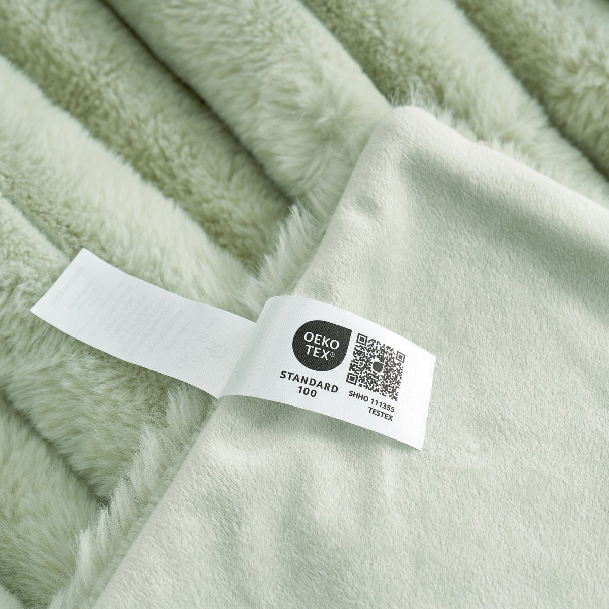 Close-up of Sage green Cozy Bliss faux fur blanket, Oeko-Tex Standard 100 certified lable. #color_Sage Green