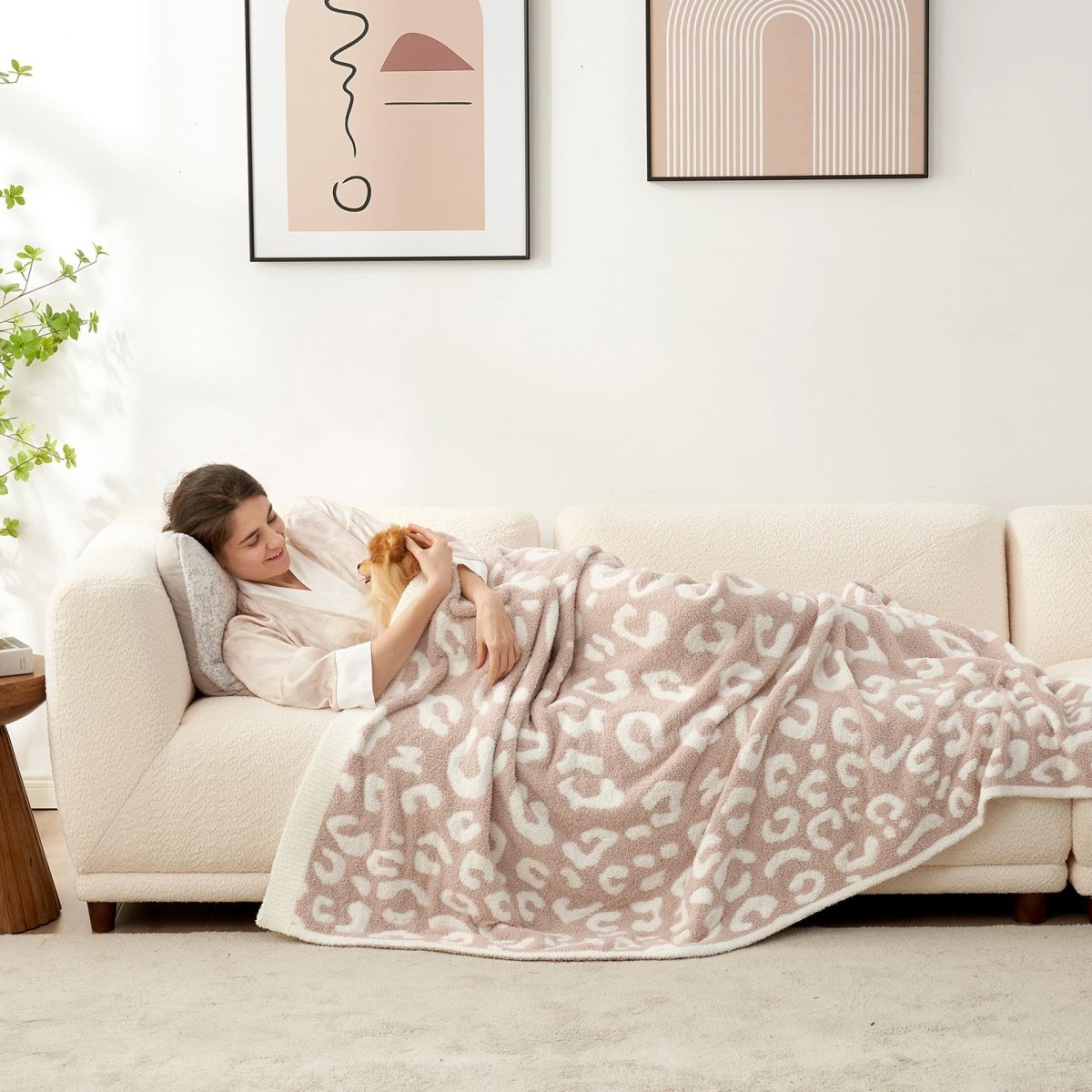 Woman with a dog relaxing on a sofa under a Reversible Leopard Feather Yarn Throw Blanket in Khaki Leopard, enjoying cozy comfort at home. #color_Khaki Leopard
