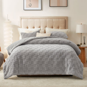 Gray quilted comforter on a bed in a bedroom setting with pillows and a lamp.